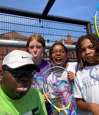 coach and 3 children posing for a photo with the racquets