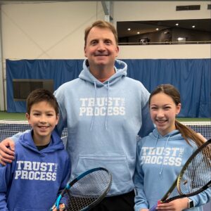 coach posing with two young tennis students
