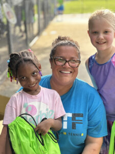 coach posing with two young tennis students
