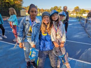 coach posing with two young tennis students
