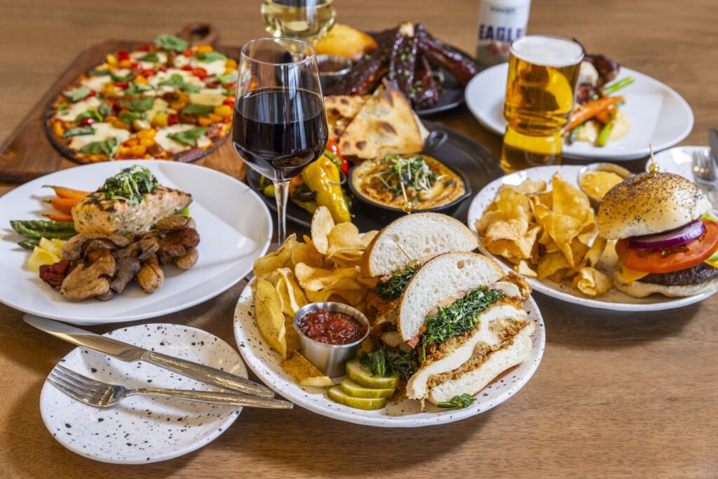 Multiple plates of food surrounding a glass of wine and a pint of beer