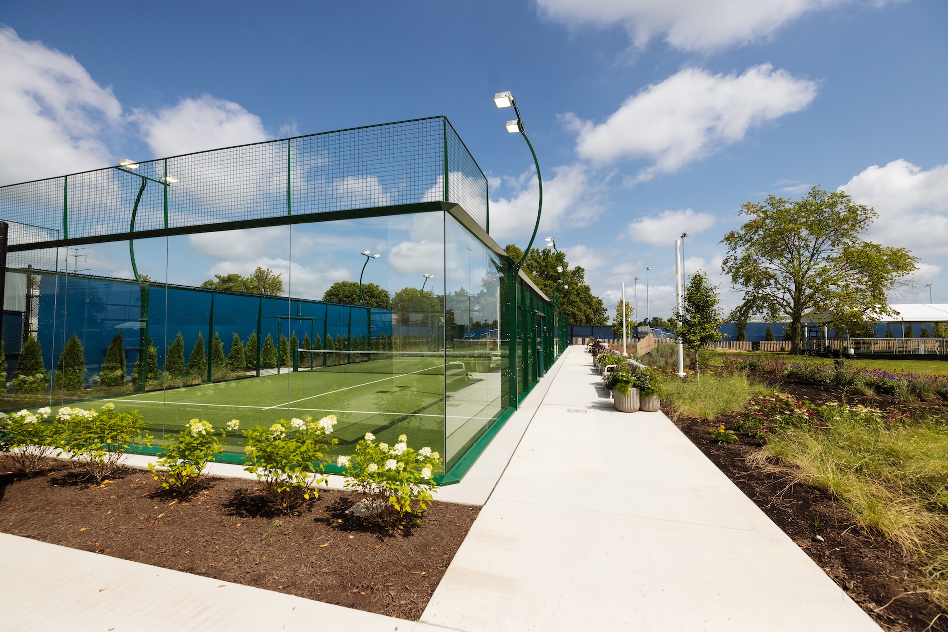 Sidewalk next to a turf padel court with greenery around it