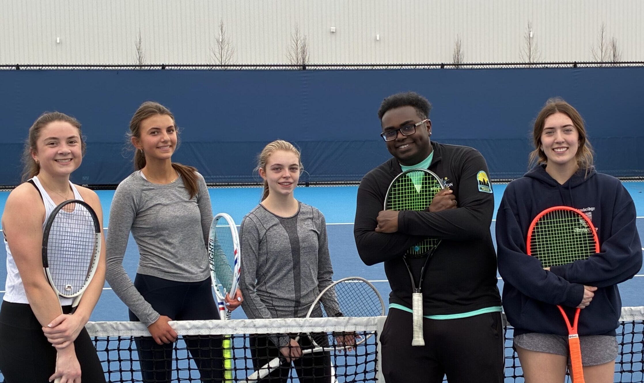 Group of people smiling at the camera holding tennis racquets at a tennis clinic